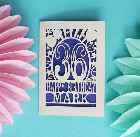 A laser cut birthday card featuring the age 36 and reads "Happy Birthday Mark". Card has a number in the centre of the design, surrounded by balloons and stars, with text underneath. The cream card is cut away to reveal a violet paper insert behind. - 