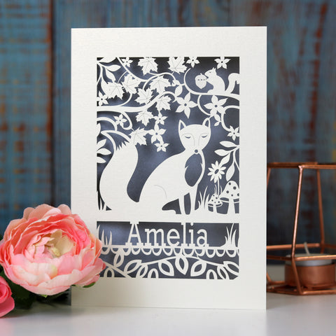 A fox birthday card, laser cut and with a silver paper insert. There is a fox in the centre, flowers and leaves around, with a squirrel and toadstool details. The name is under the fox. - A5 (large) / Silver