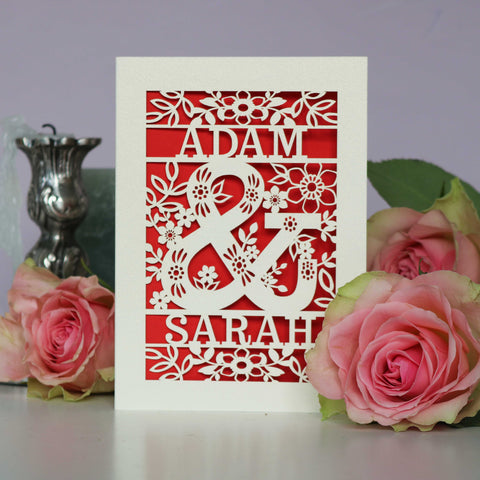 A cream laser cut wedding card with a red paper insert. Card has two names and a large, floral ampersand, with flowers and leaves around it. - A5 / Bright Red