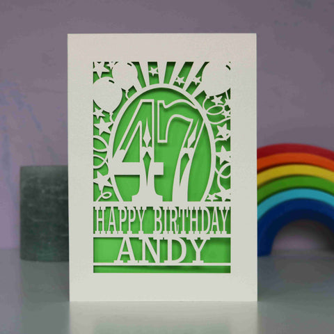 A cream paper cut birthday card cut away to reveal a green background. Cut design is an age surrounded by stars and balloons, with the words "Happy birthday" and a name underneath - A5 (large) / Bright Green