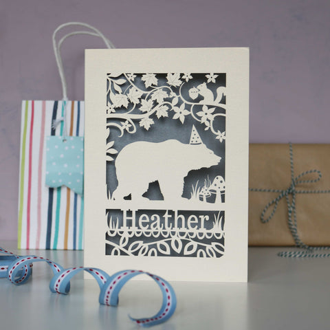 Papercut bear design birthday card.  Shows a bear wearing a hat, walking under a tree with a squirrel. Can be personalised with a name and age if you wish. Cut from cream card with a silver insert. - A5 (large) / Silver