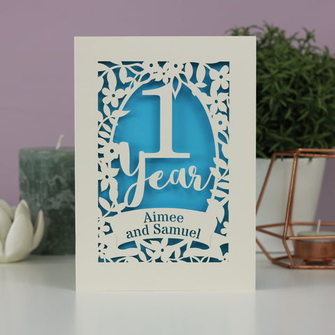 A 1st anniversary card with names in a banner and a flower border. - A5 (large); / Peacock Blue;