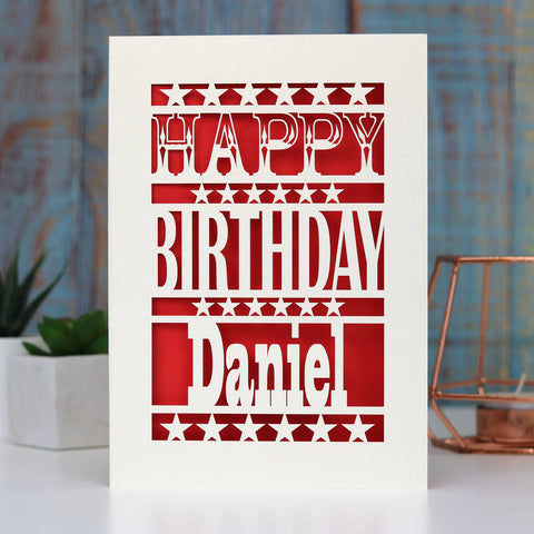 A birthday card with stars and the words Happy Birthday in cream and a name underneath. Red paper sits behind the laser cut design - A5 / Bright Red