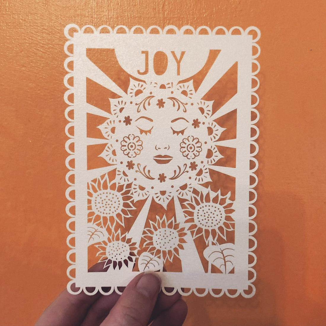 A laser cut postcard with the sun and the word "Joy" against an orange background