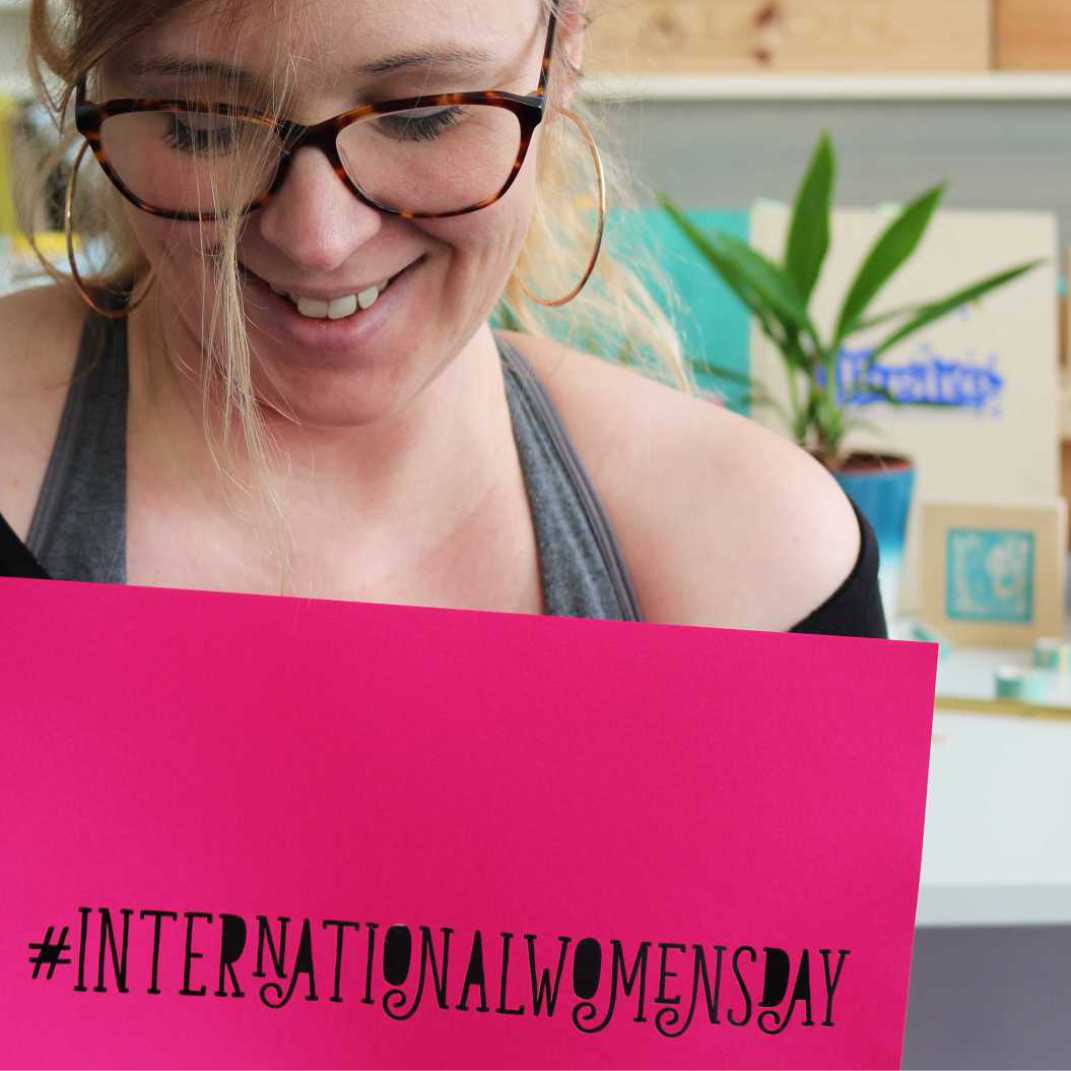 Emma holding a bright pink piece of paper with laser cut words International Women's Day