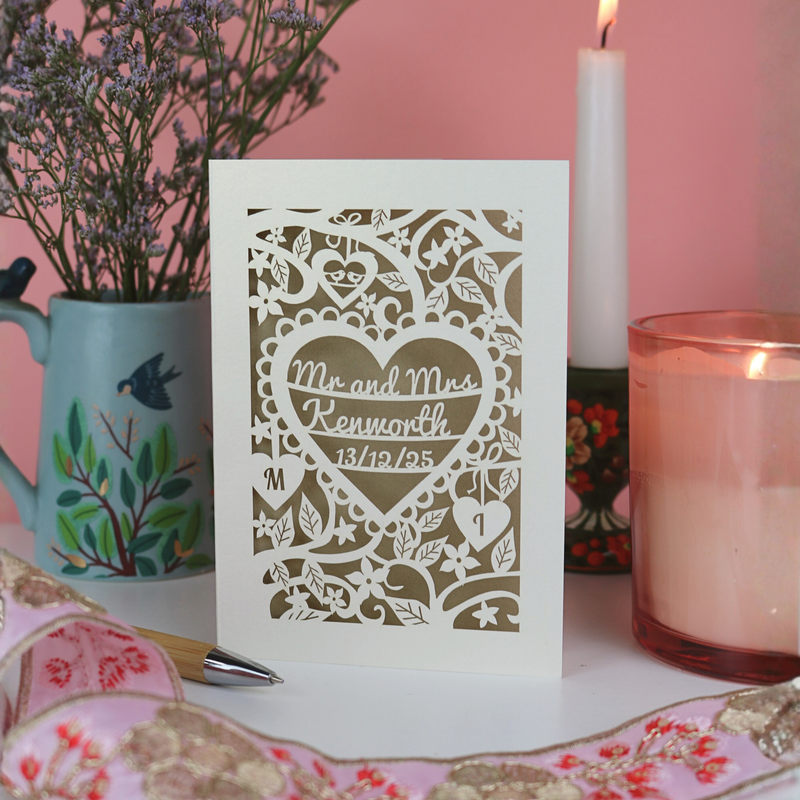 A laser cut wedding card on a pink background