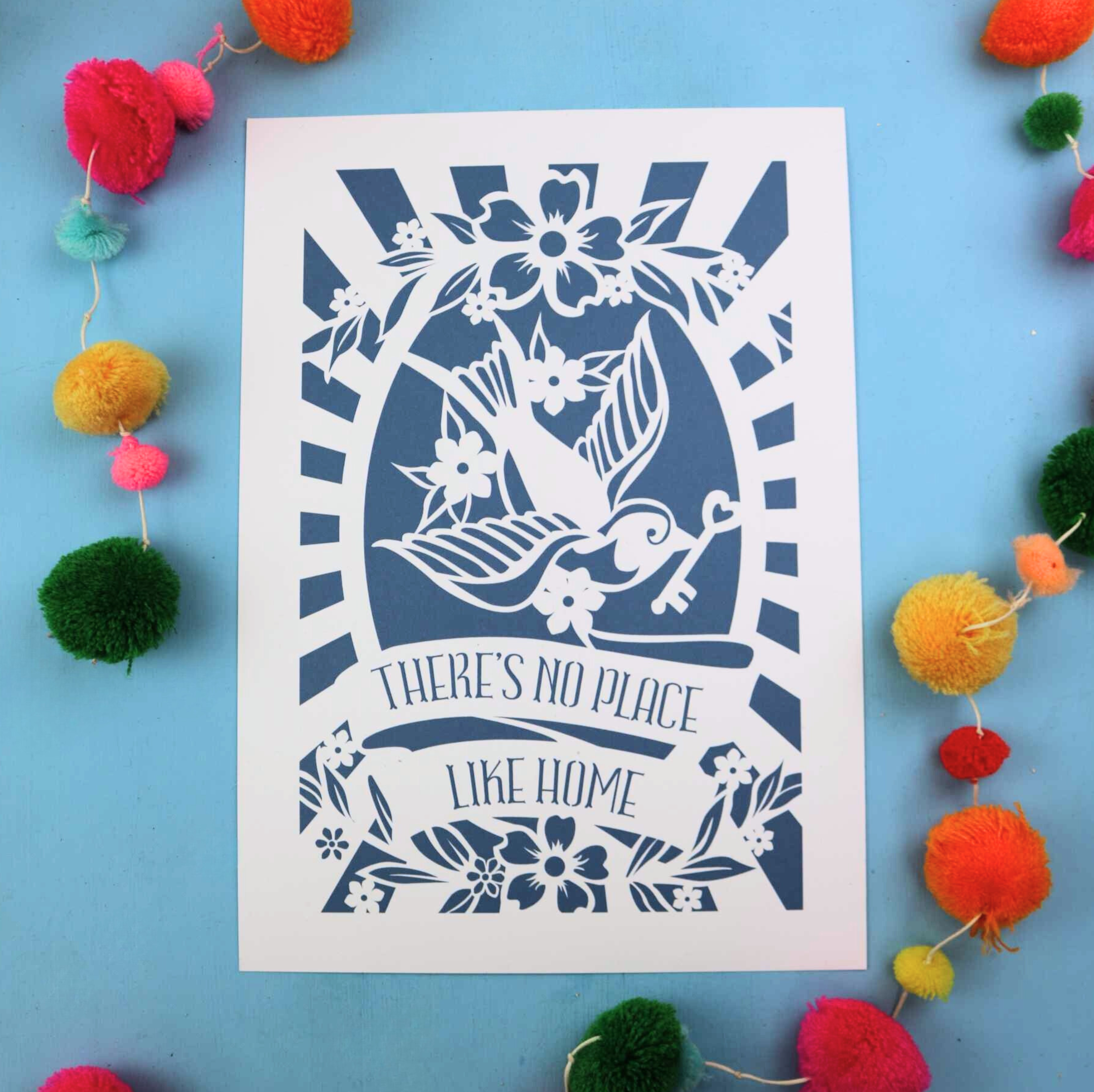 A blue and white A4 wall art print in a papercut style featuring a swallow holding a key and the words "There's no place like home"