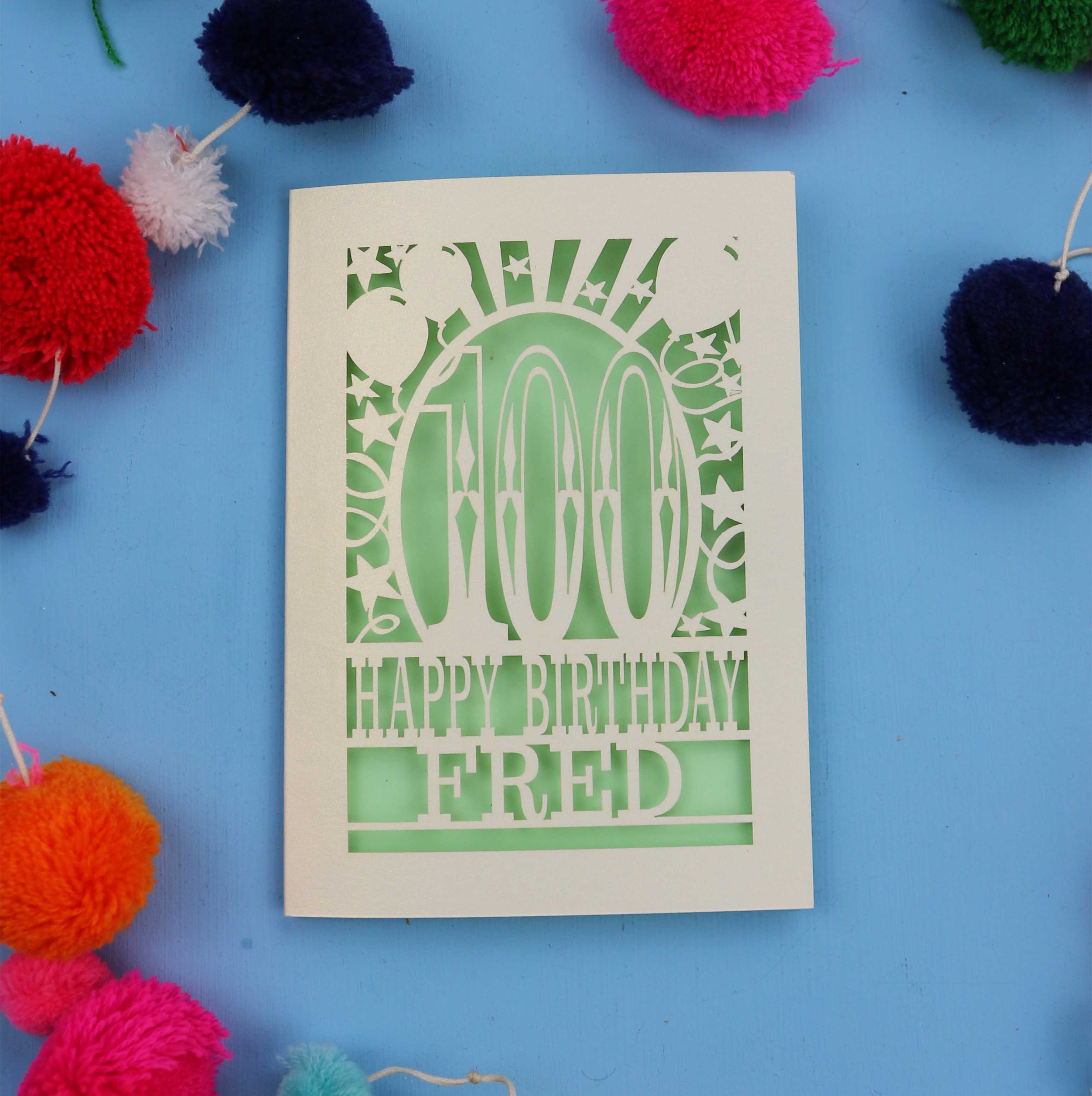 Keepsake 100th Birthday card with 'Happy Birthday Fred' text on a blue background with colourful pom-poms.