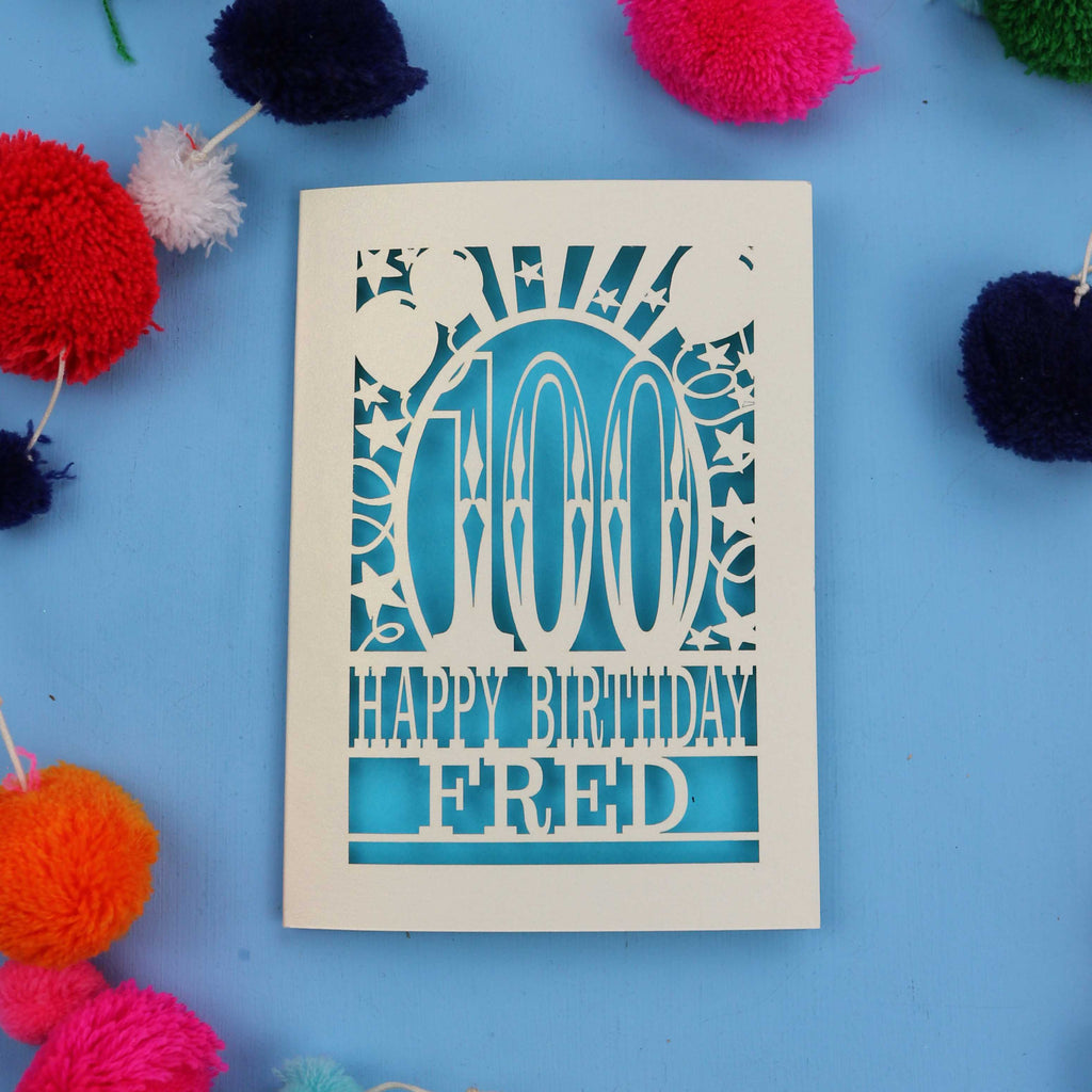 Laser Cut 100th Birthday card with 'Happy Birthday Fred' text on a blue background with colourful pom-poms.