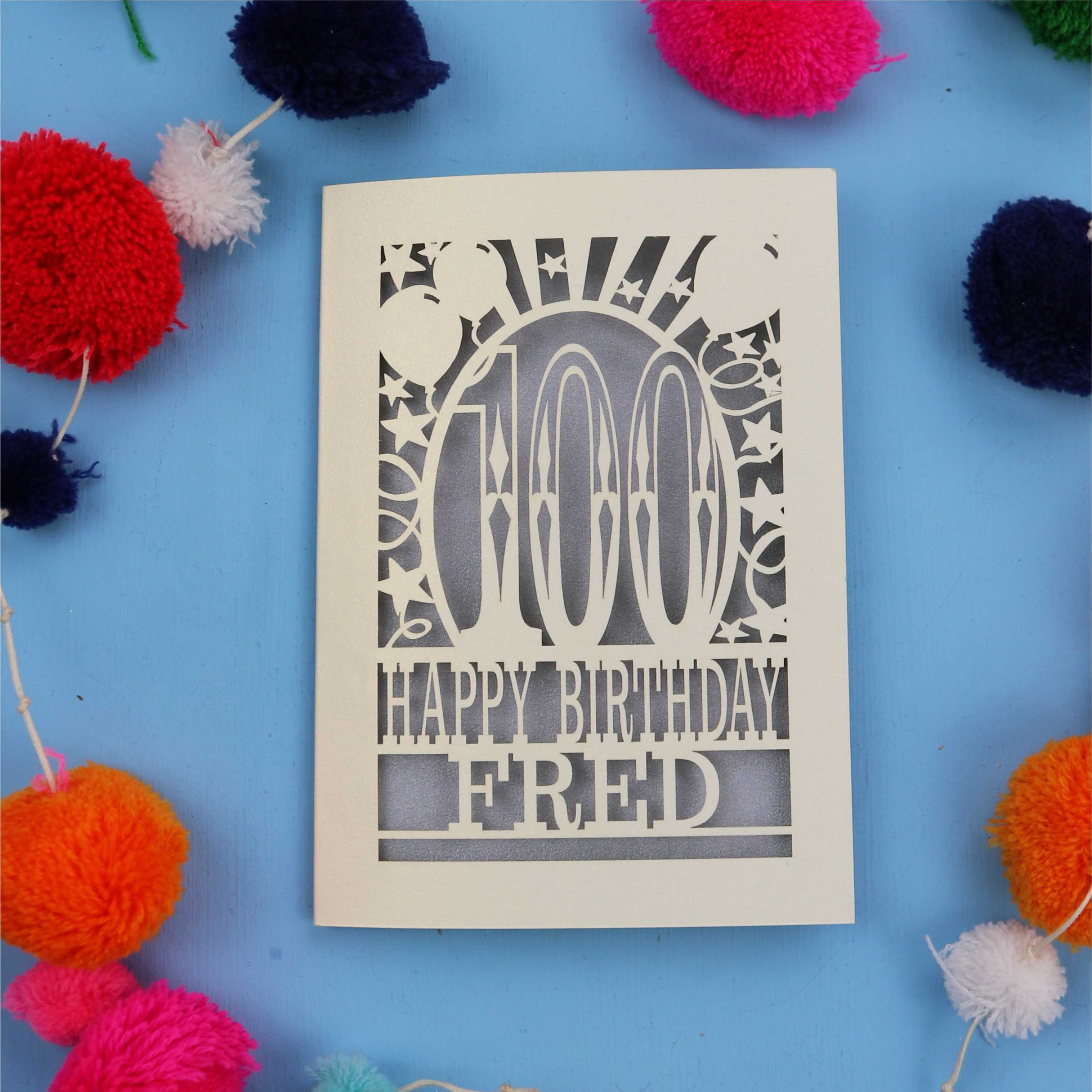 100th Birthday card with 'Happy Birthday Fred' text on a blue background with colourful pom-poms.