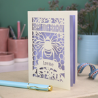 Personalized 100 birthday card with cut out  bee design on a desk with stationery items.