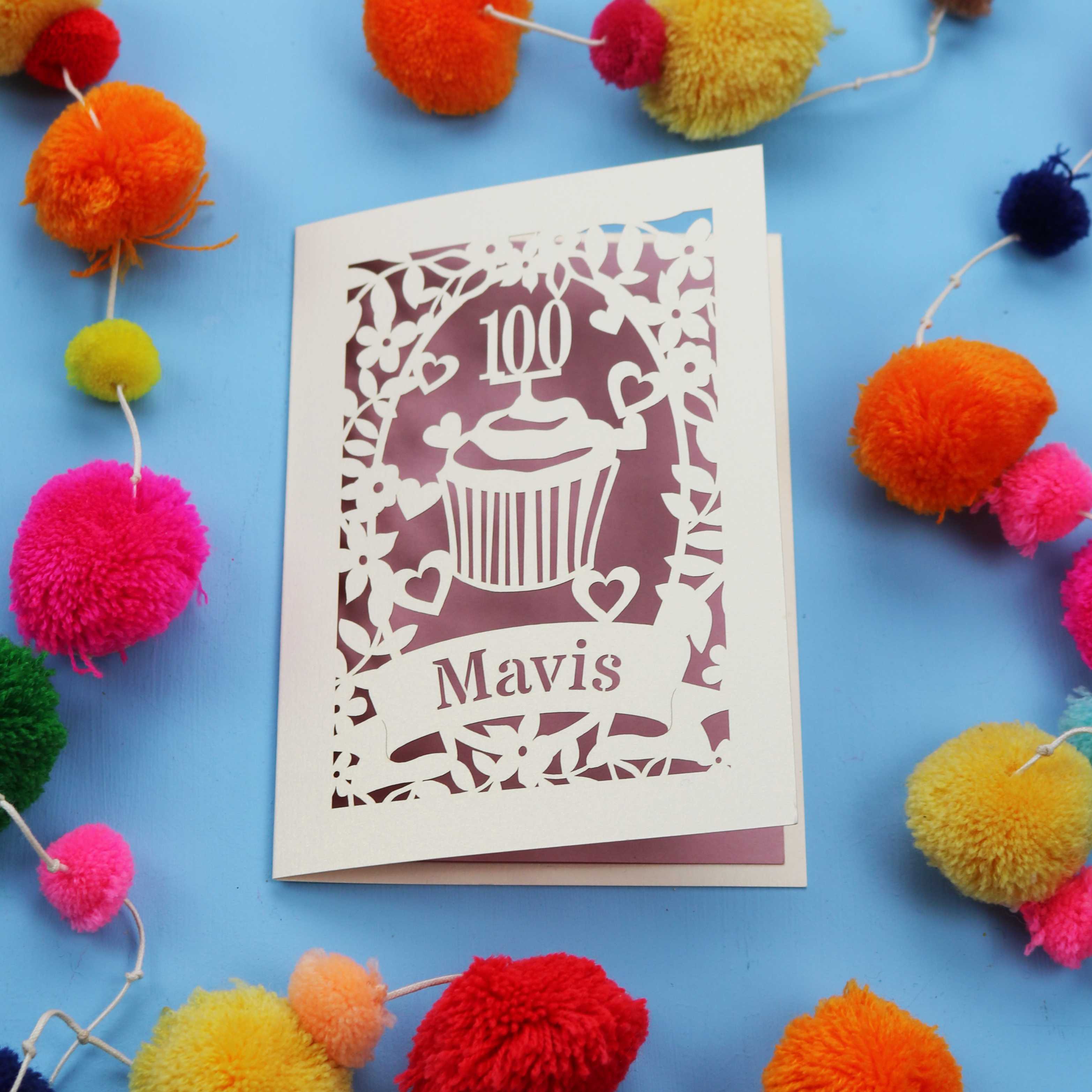 laser cut 100th card with '100 Mavis' design on a blue background with colourful pom-poms.