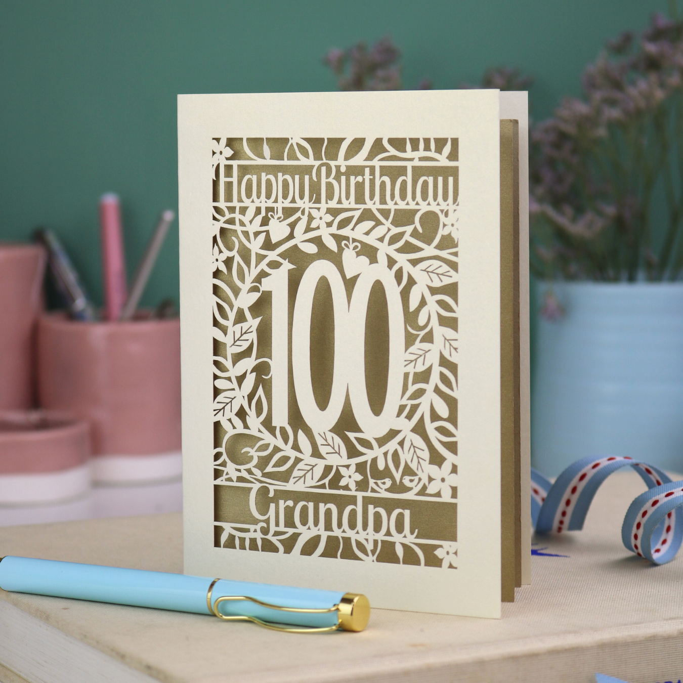 A laser cut 100th birthday card with floral '100' cut out design, 'Happy Birthday' text, and personalised with a name. 