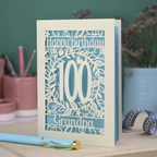 A laser cut 100th birthday card with floral '100' cut out design, 'Happy Birthday' text, and personalised with a name. 