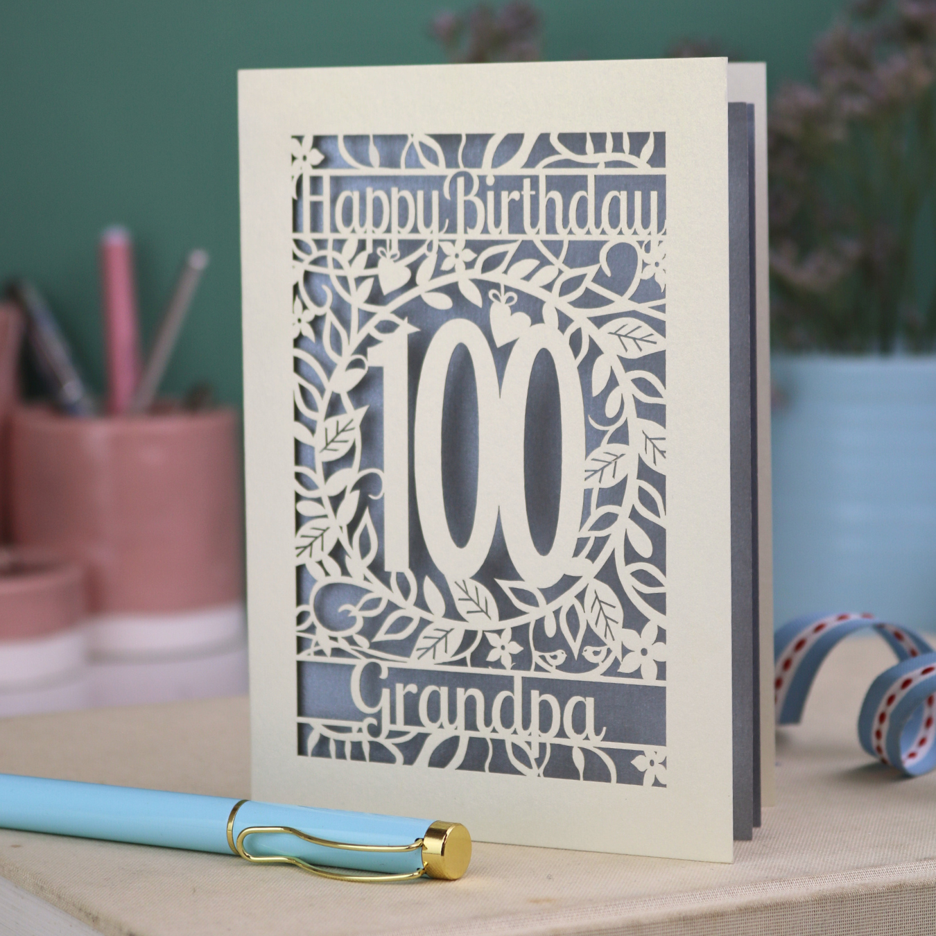 A laser cut 100th birthday card with floral '100' cut out design, 'Happy Birthday' text, and personalised with a name. 
