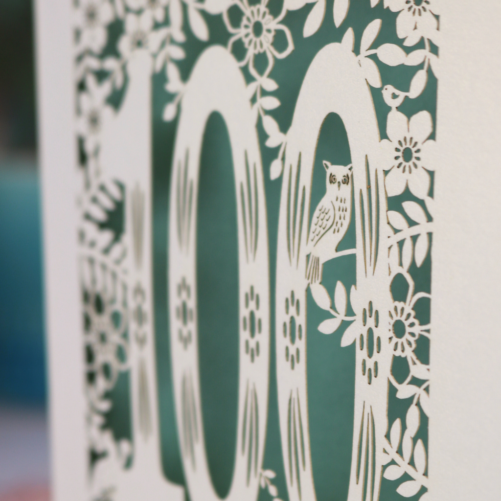 Decorative paper cutout with an owl and floral patterns on a green background