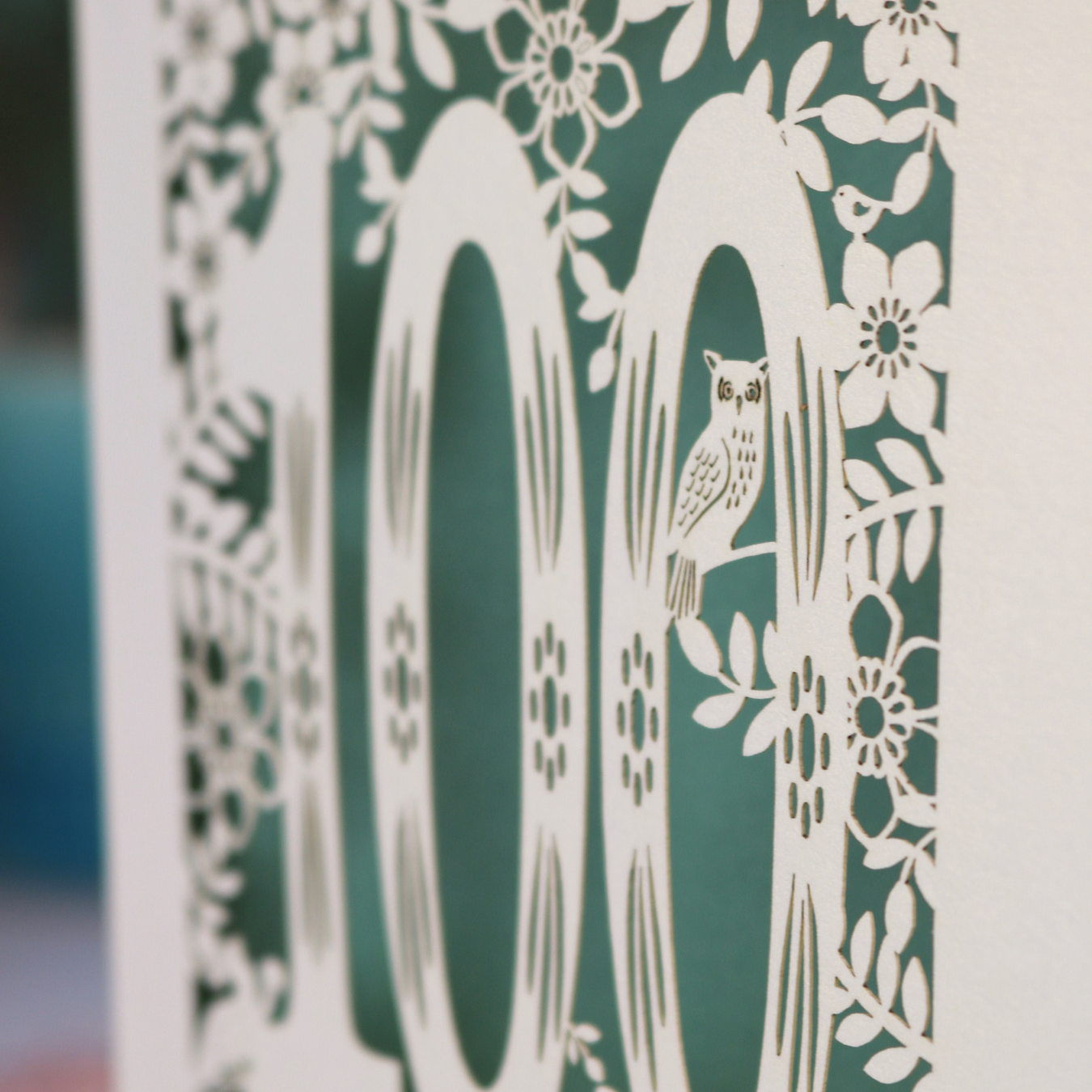 Decorative paper cutout with an owl and floral patterns on a green background
