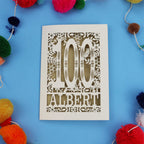 Decorative paper cut out 100th birthday card with '100 Albert' on a blue background with colourful pom-poms.