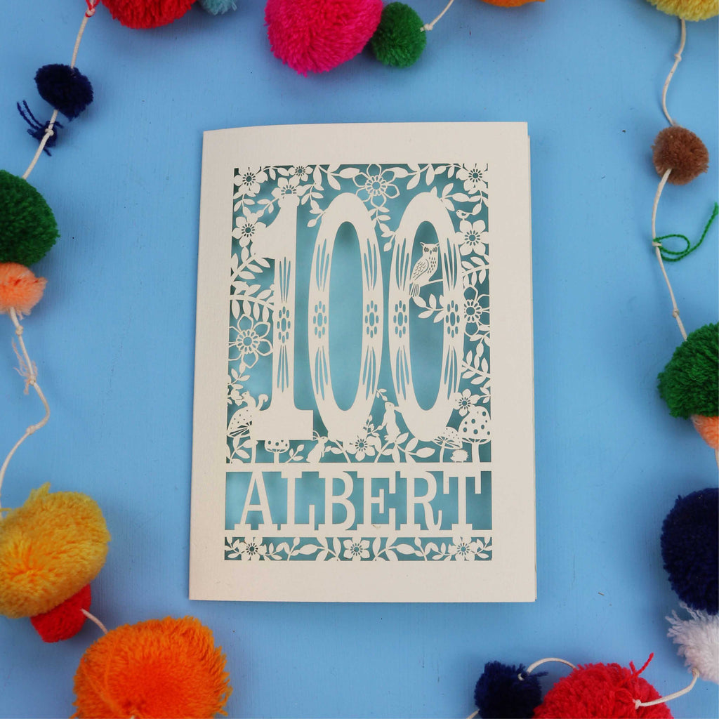 Decorative paper cut out 100th birthday card with '100 Albert' on a blue background with colourful pom-poms.