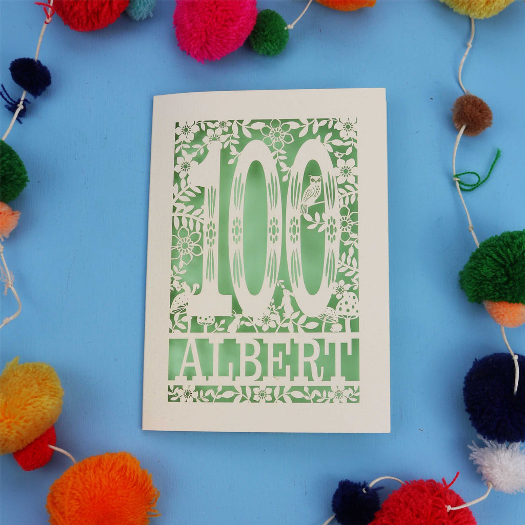 Decorative paper cut out 100th birthday card with '100 Albert' on a blue background with colourful pom-poms.