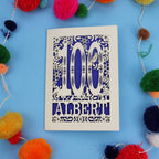 Decorative paper cut out 100th birthday card with '100 Albert' on a blue background with colourful pom-poms.