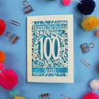 Laser cut 100th birthday card with decorative elements on a blue background