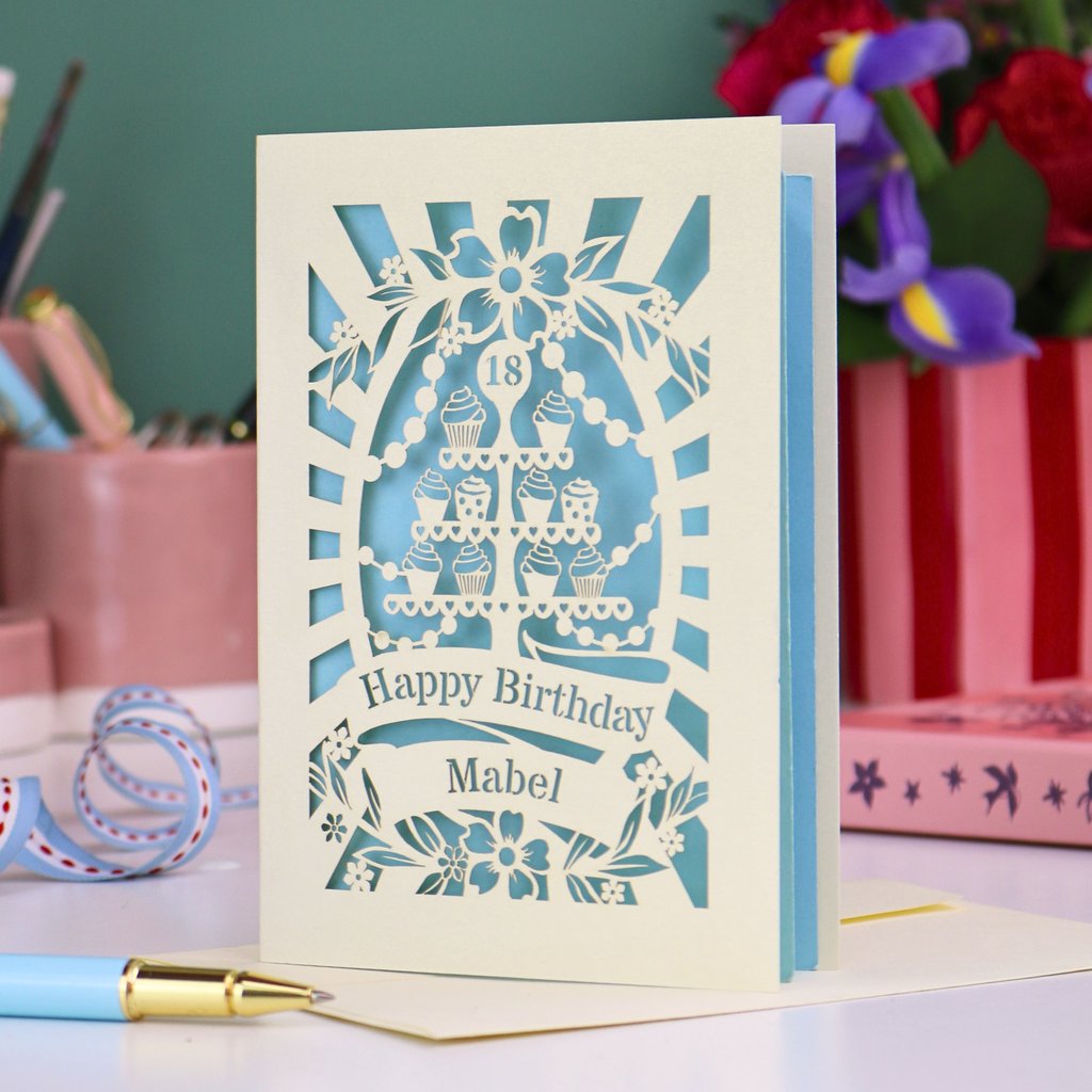 Laser-cut 18th birthday card with blue design on a desk with stationery items.