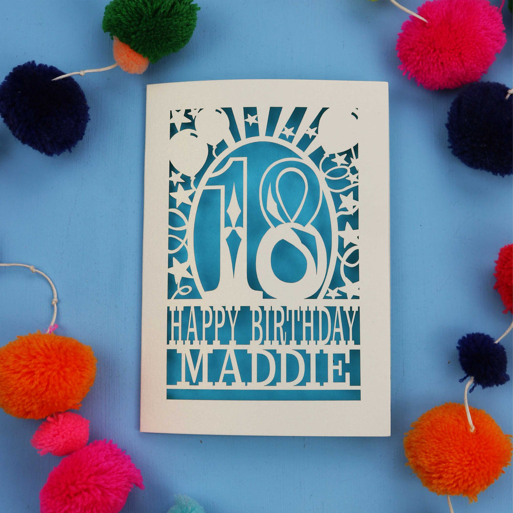 18th Birthday card with 'Happy Birthday Maddie' on a blue background with colourful pom-poms