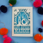 18th Birthday card with 'Happy Birthday Maddie' on a blue background with colourful pom-poms