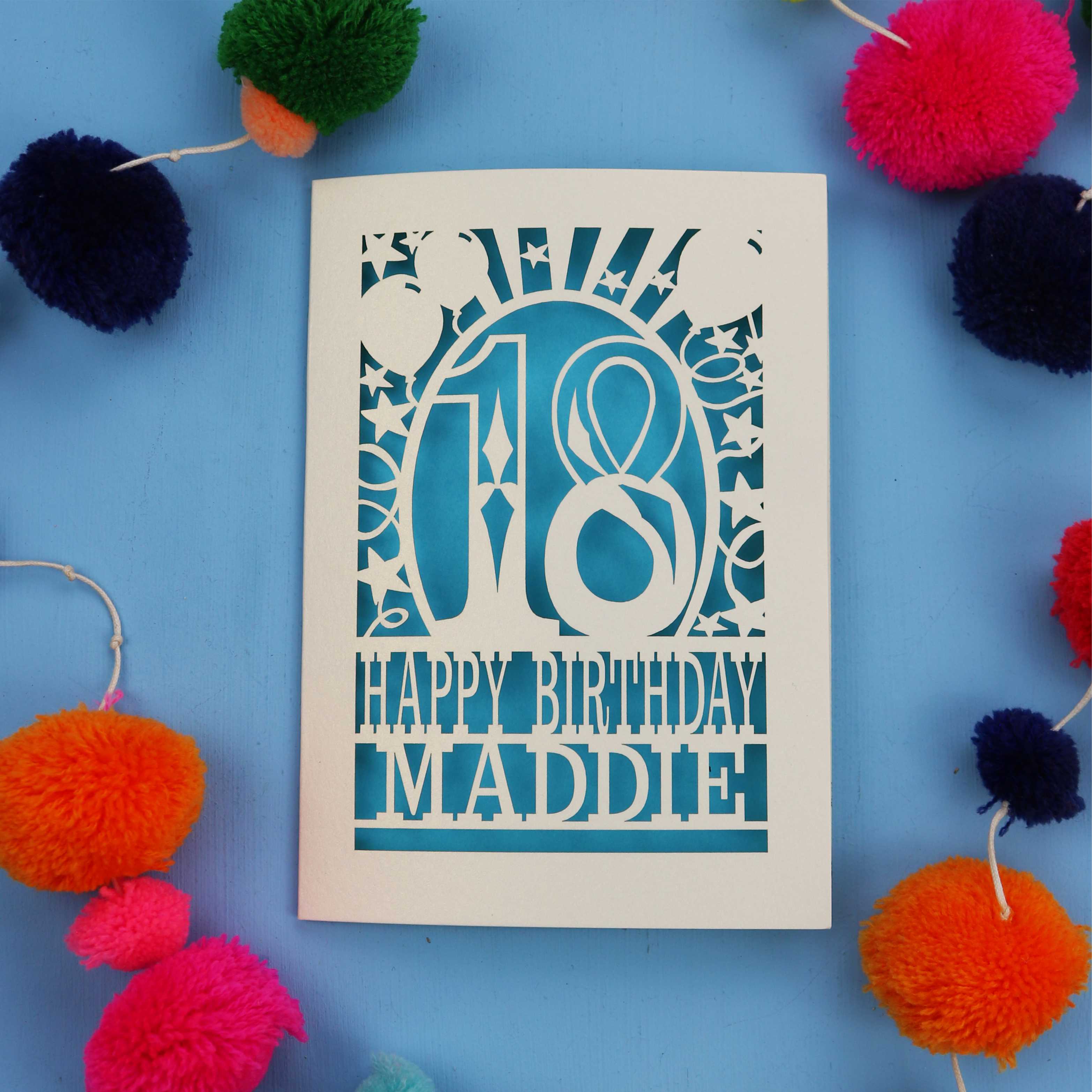 18th Birthday card with 'Happy Birthday Maddie' on a blue background with colourful pom-poms
