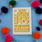 18th Birthday card with 'Happy Birthday Maddie' on a blue background with colourful pom-poms