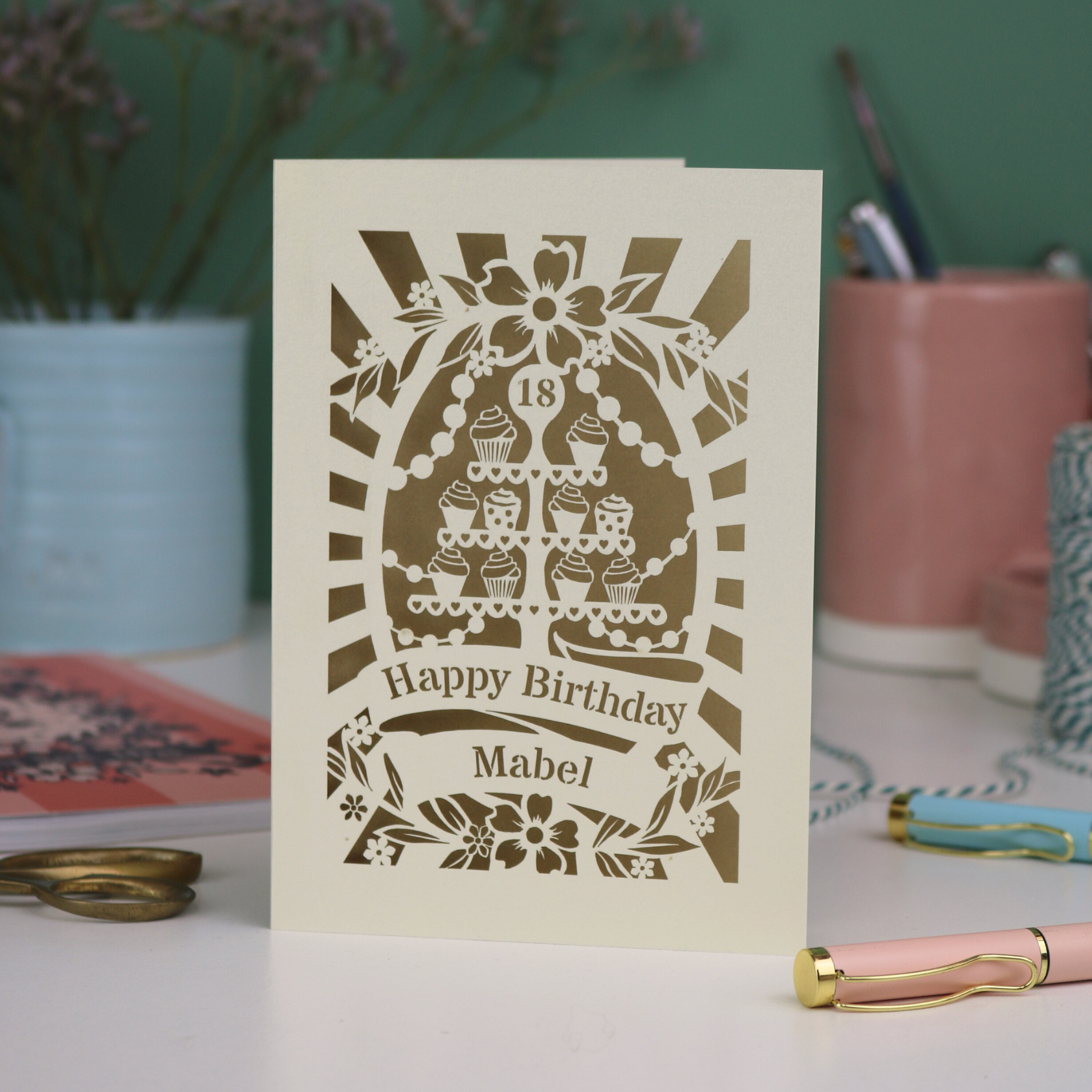 Personalised and laser cut 18th Birthday card with decorative cupcake stand design on a table with stationery items.
