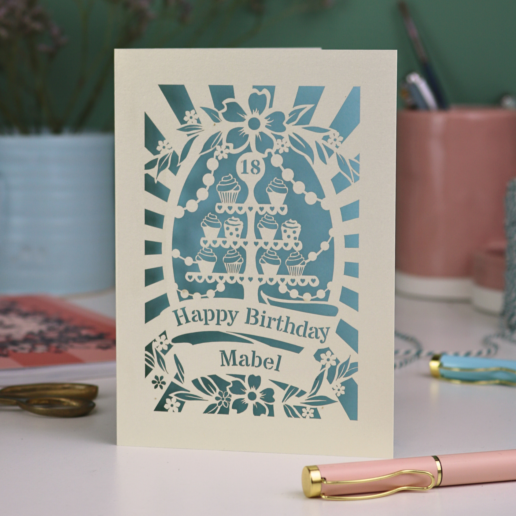 Personalised and laser cut 18th Birthday card with decorative cupcake stand design on a table with stationery items.