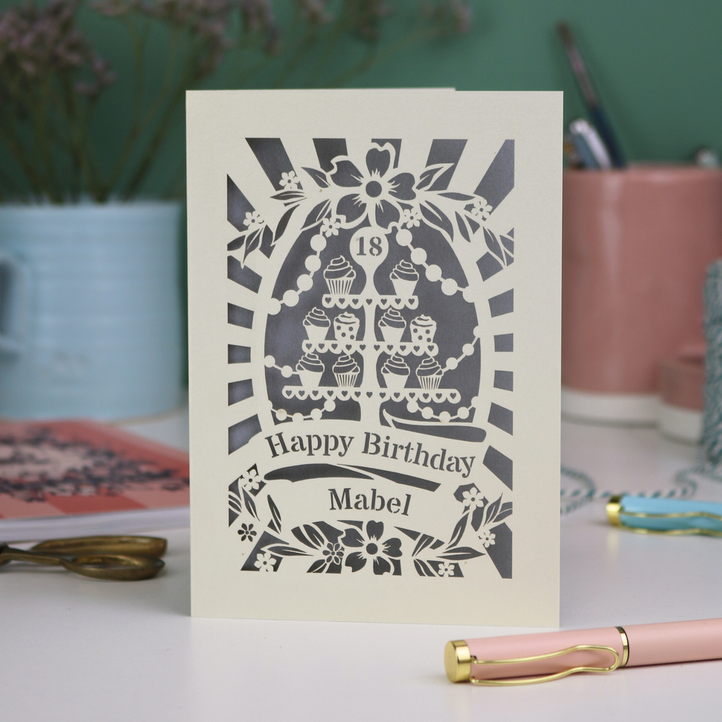 Personalised and laser cut 18th Birthday card with decorative cupcake stand design on a table with stationery items.