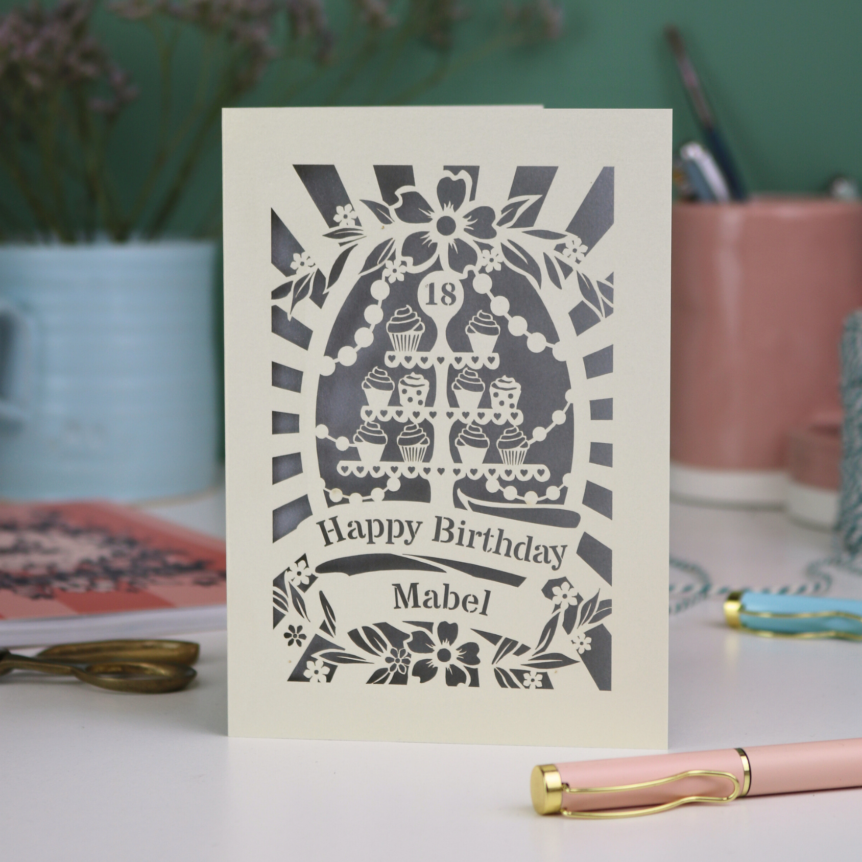 Personalised and laser cut 18th Birthday card with decorative cupcake stand design on a table with stationery items.