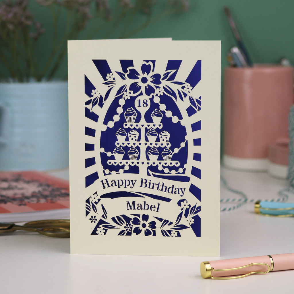 Personalised cut out 18th Birthday card with decorative cupcake stand design on a table with stationery items.