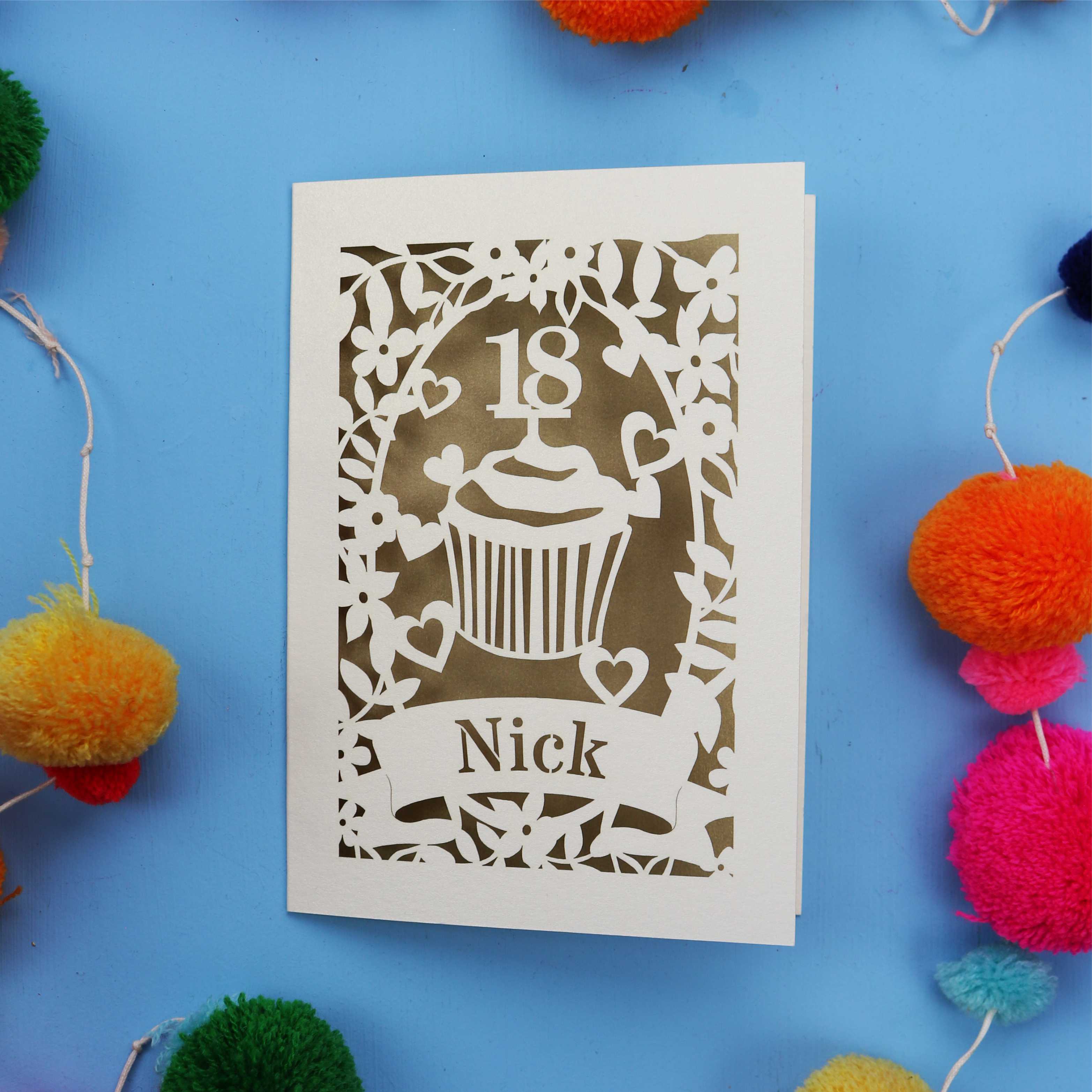 Decorative 18th birthday card with cut-out design on a blue background with colourful pom-poms.