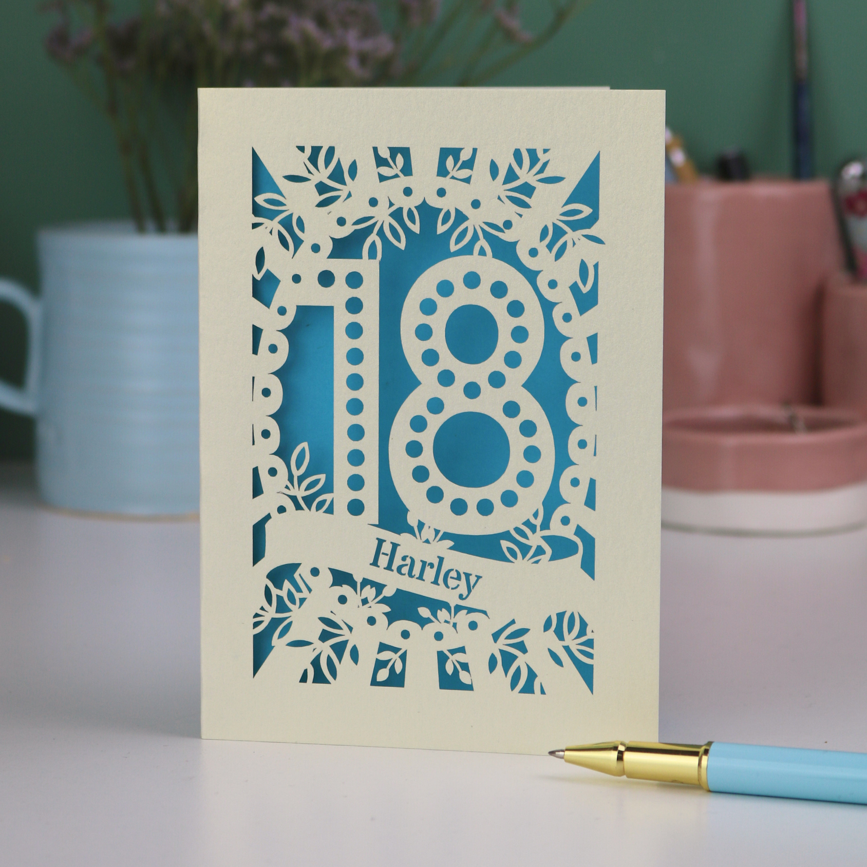 Card with '18' and 'Harley' on a table with a pen and plant in the background
