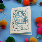 Decorative 18th birthday card with cut-out design on a blue background with colourful pom-poms.