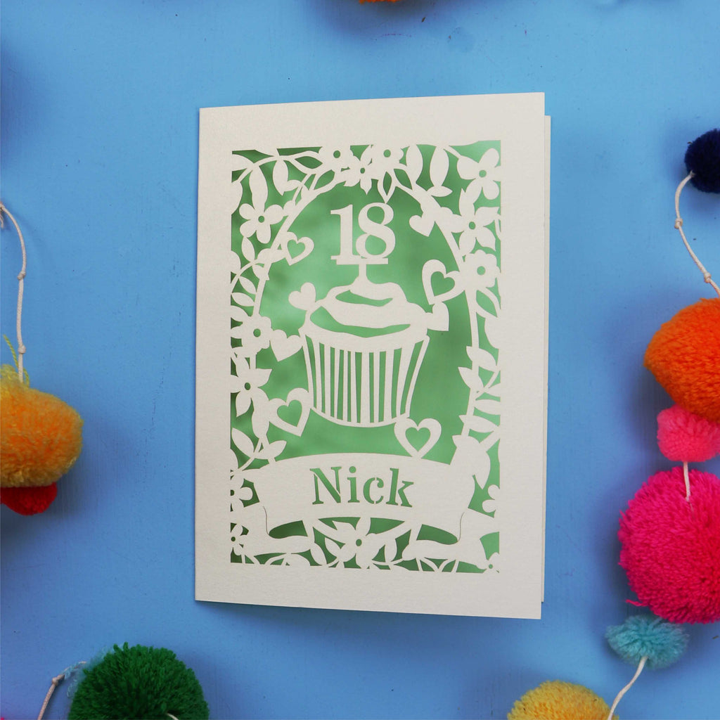 Decorative 18th birthday card with cut-out design on a blue background with colourful pom-poms.