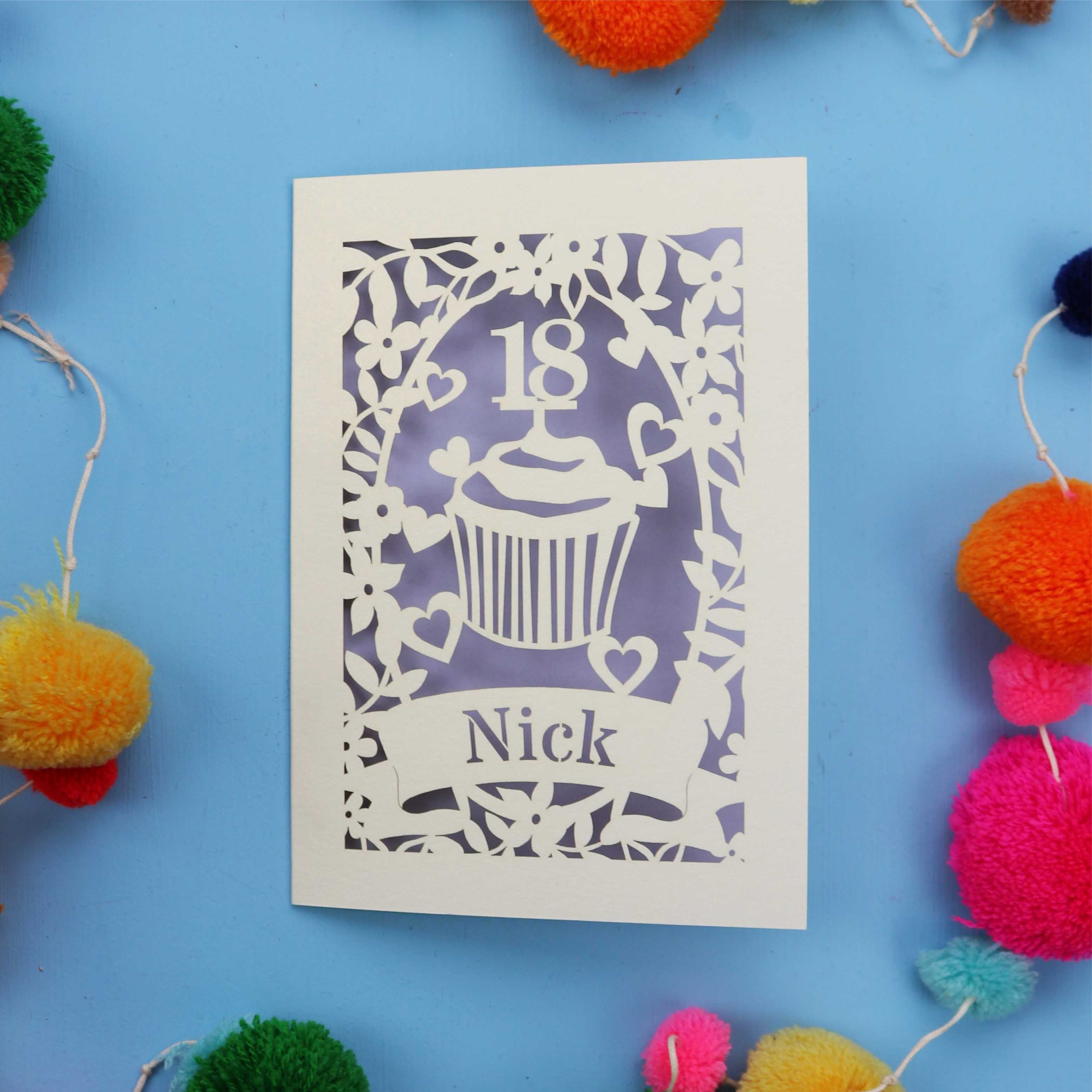 Decorative 18th birthday card with cut-out design on a blue background with colourful pom-poms.