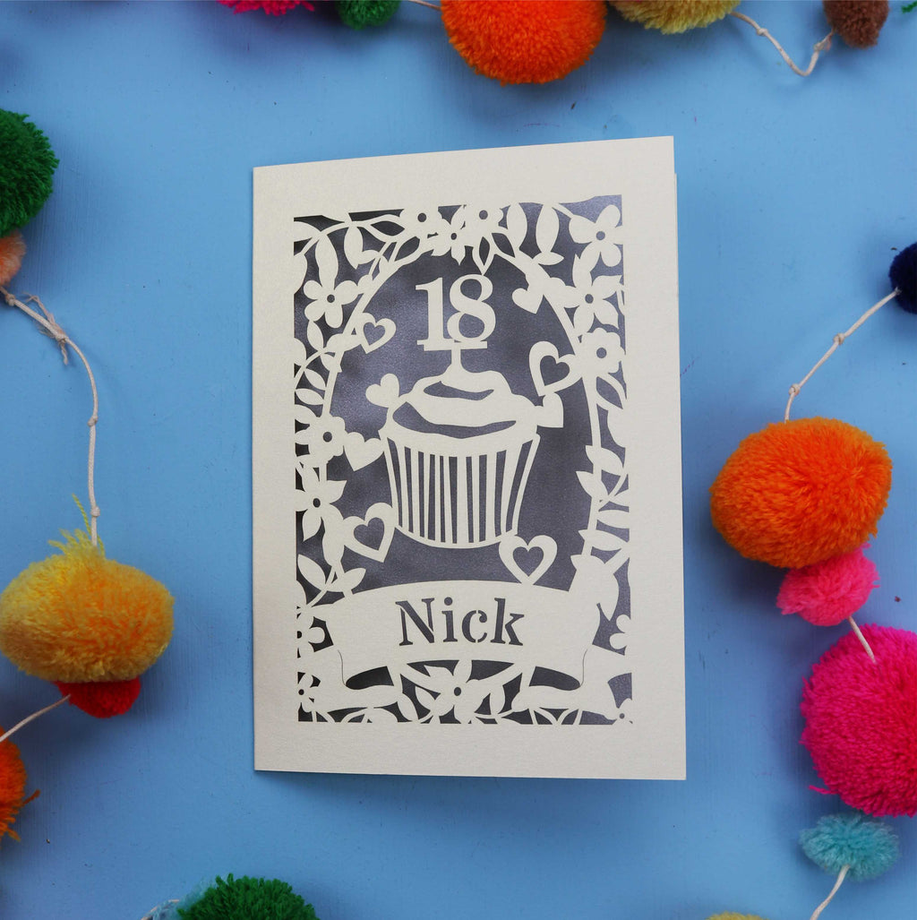 Decorative 18th birthday card with cut-out design on a blue background with colourful pom-poms.