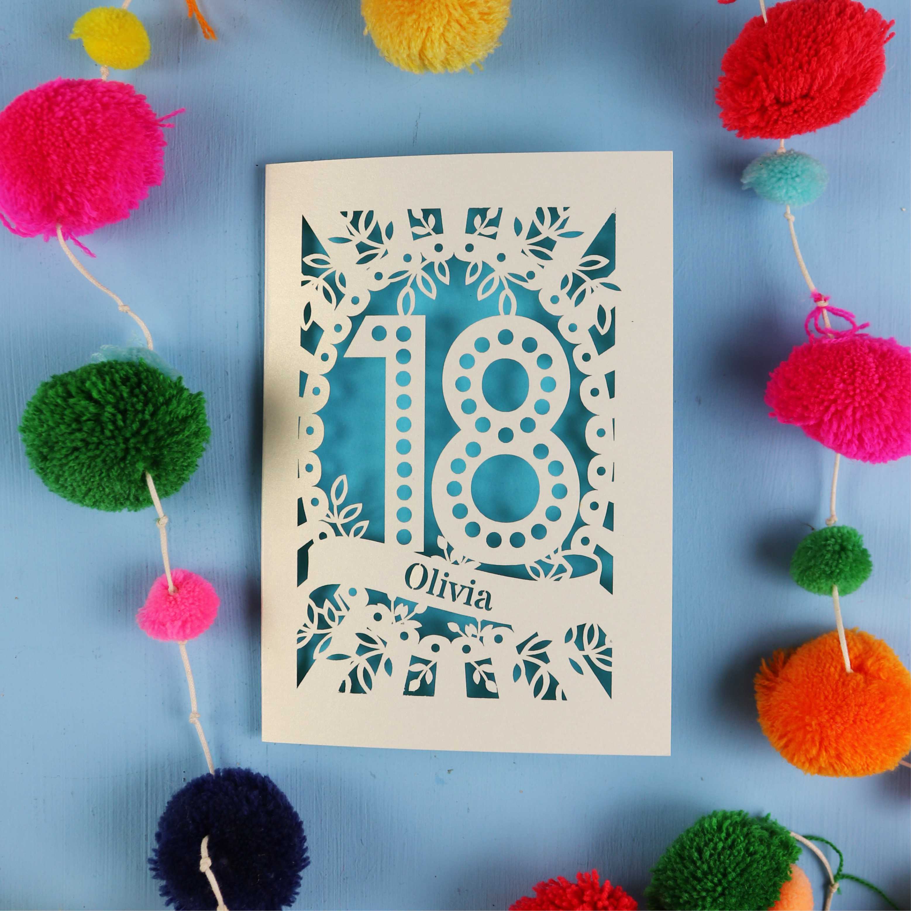 Decorative 18th birthday card with '18' and 'Olivia' on a blue background with colourful pom-poms.