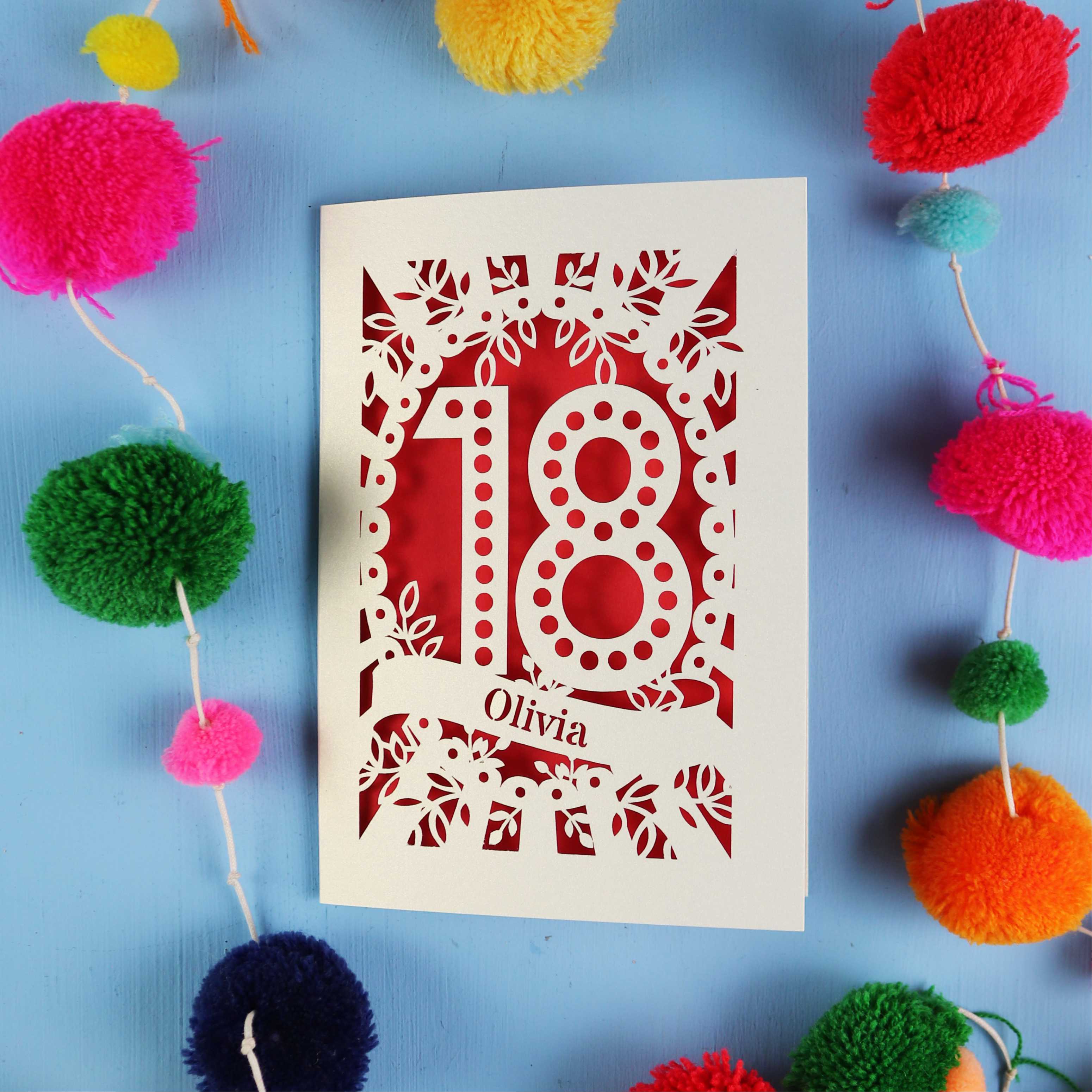 Decorative 18th birthday card with '18' and 'Olivia' on a blue background with colourful pom-poms.