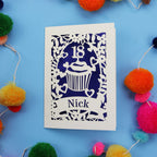 Decorative 18th birthday card with cut-out design on a blue background with colourful pom-poms.