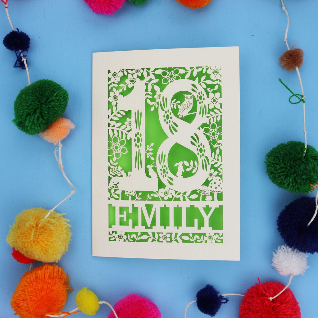 Personalised 18th birthday card  with floral patterns and 'EMILY' text on a blue background with colourful pom-poms.