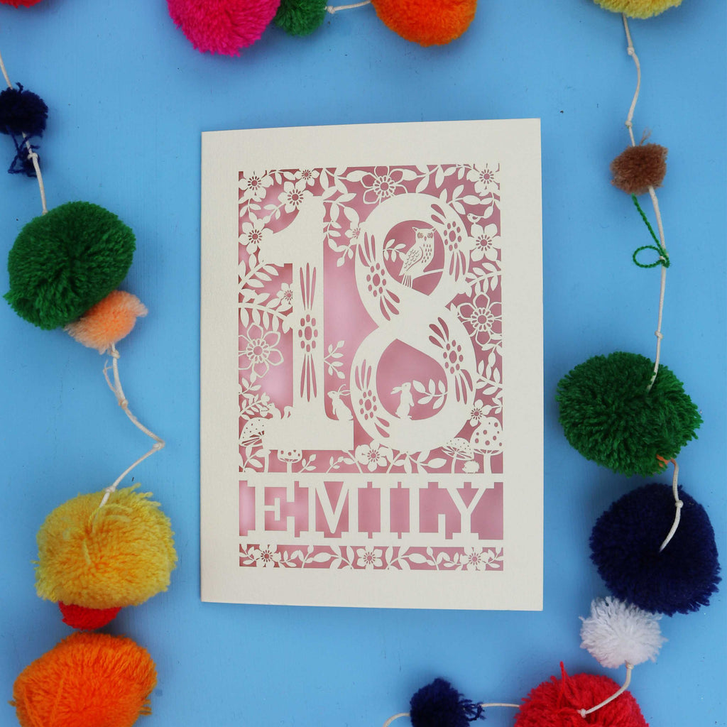 Laser cut 18th birthday card with floral patterns and 'EMILY' text on a blue background with colourful pom-poms.