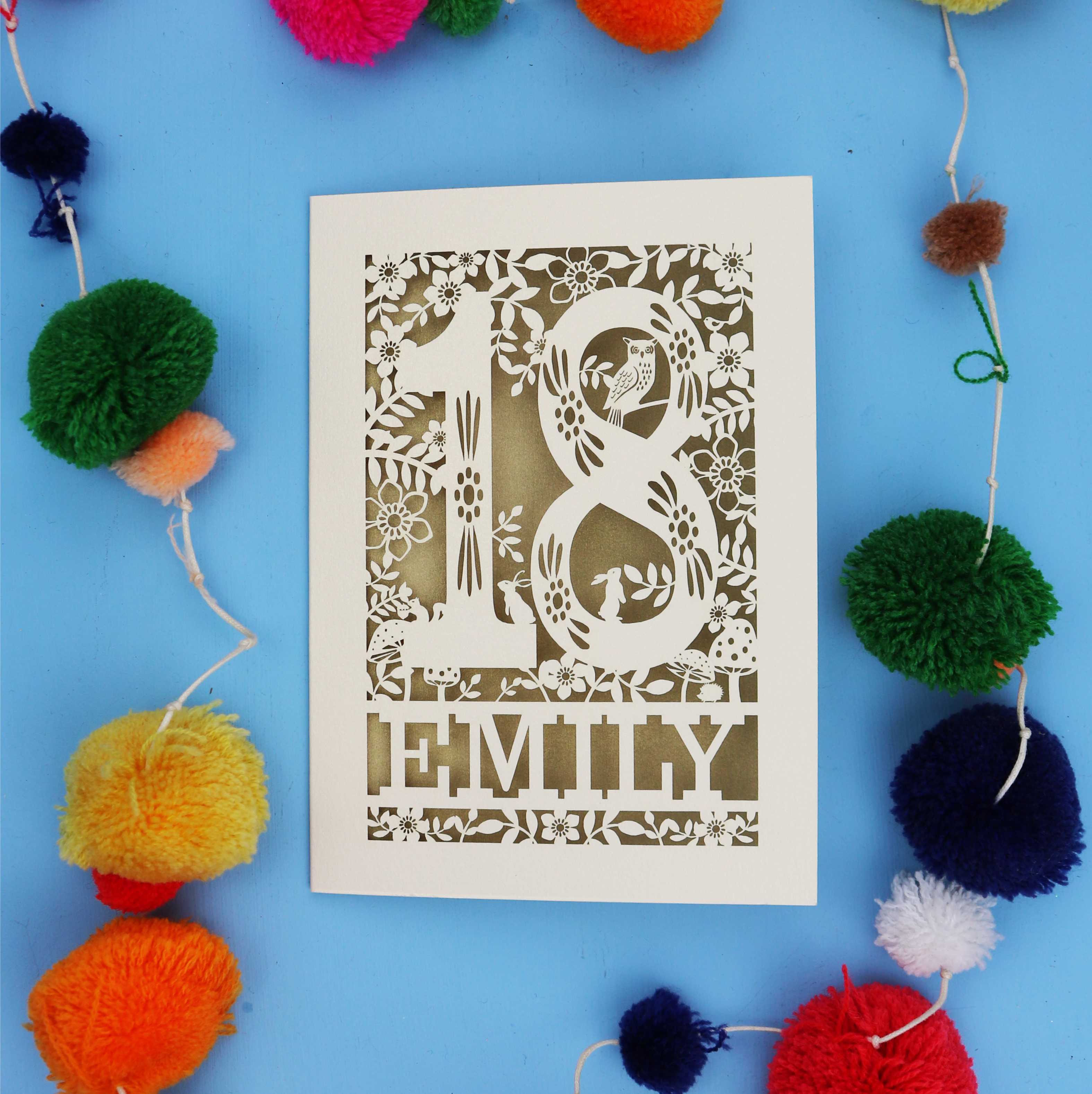 Unique 18th birthday card with floral patterns and 'EMILY' text on a blue background with colourful pom-poms.