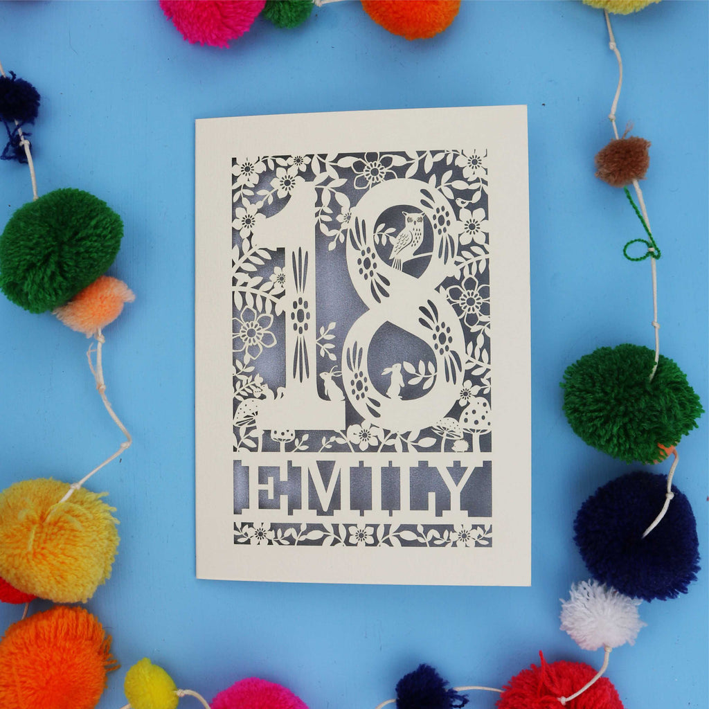 Woodland 18th birthday card  with floral patterns and 'EMILY' text on a blue background with colourful pom-poms.