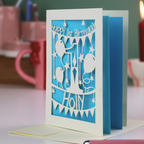 Birthday card with cut-out design and 'Happy 1st Birthday Holly' text on a blue background.